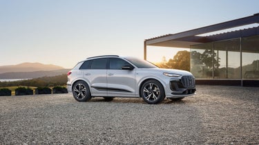 Three-quarter side view of the Audi Q6 e-tron parked by a modern home.