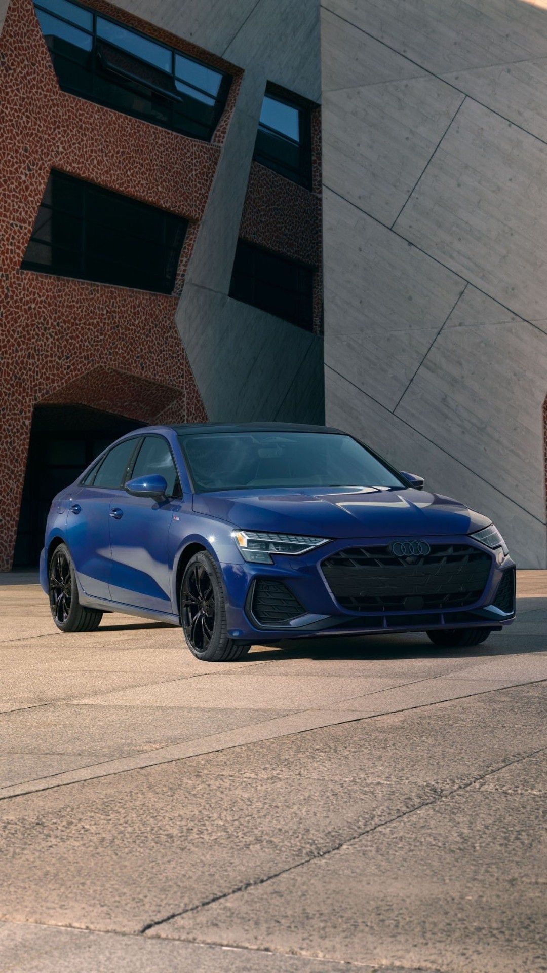 Three quarter front view of a blue Audi A3 parked in front of building.