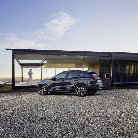Three-quarter side view of the Audi Q6 e-tron parked in front of a modern building.