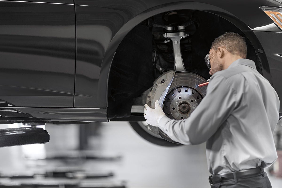 A technician inspecting the front brake rotor and caliper on a raised Audi