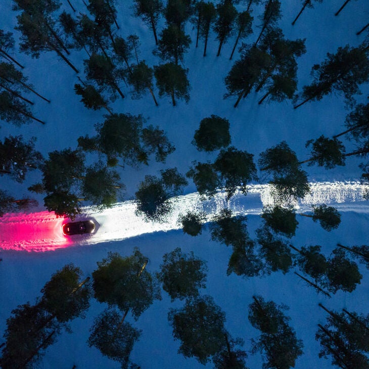 Aerial view of an Audi e-tron driving through a snowy forest at twilight. 