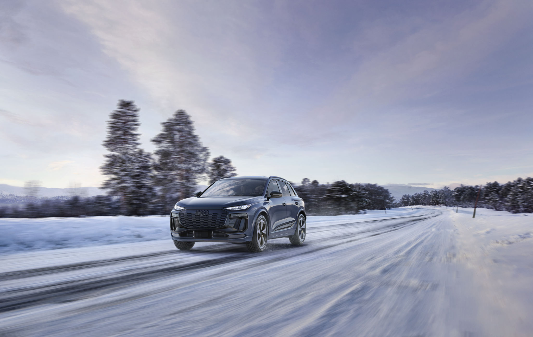 Black 2027 q6 e-tron driving on light snow with trees in the background. 