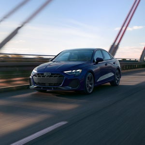 A three-quarter front view of an Audi A3 driving on a bridge.