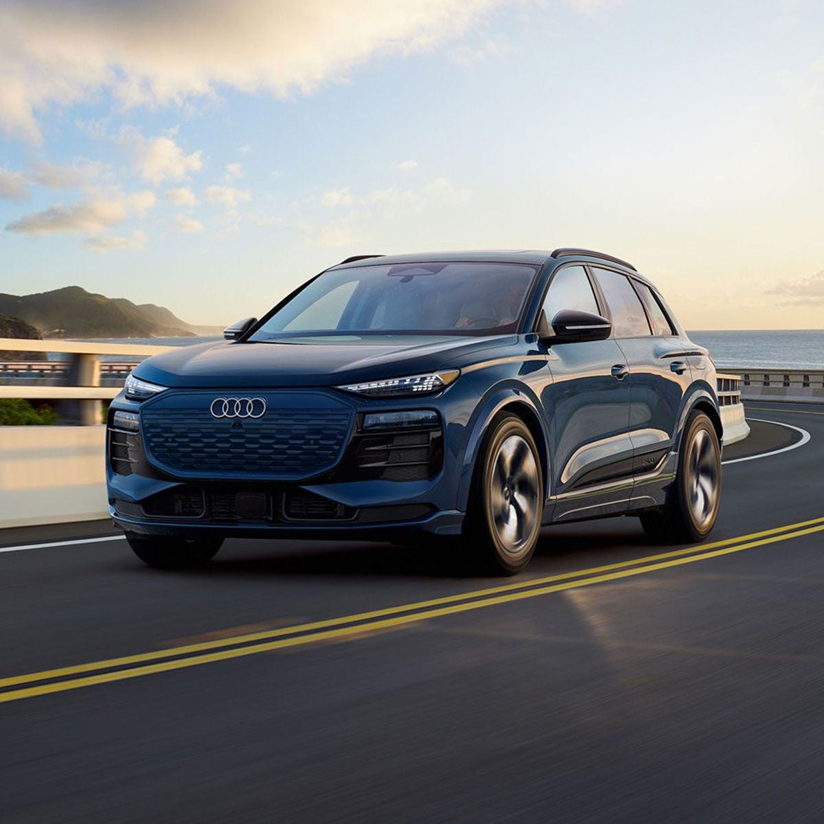 Front 3/4 shot of the 2025 Audi Q6 e-tron driving on bridge.