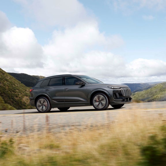 Plan latéral en plongée d’un Audi SQ6 e-tron gris qui accélère sur une colline.