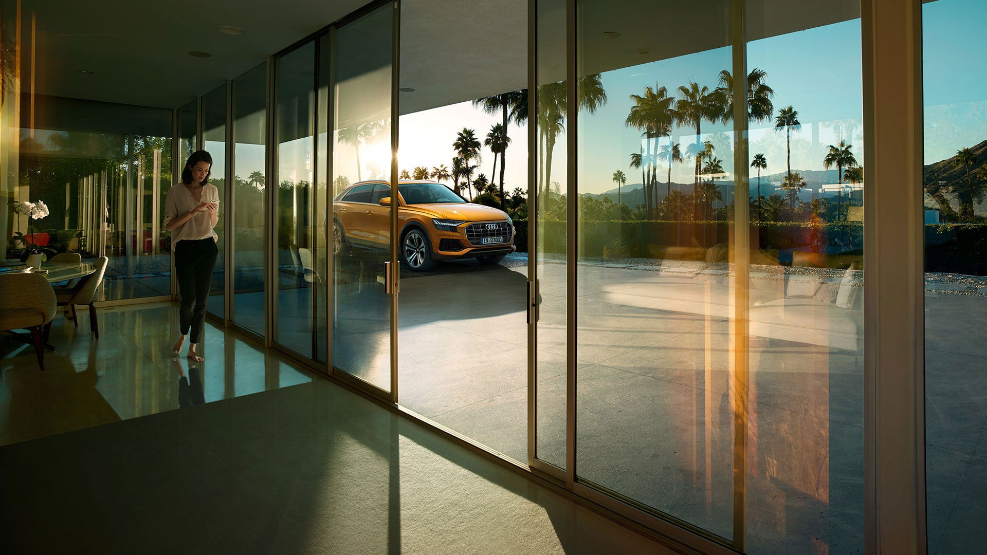 Woman looking at phone with orange Audi Q6 parked outside.