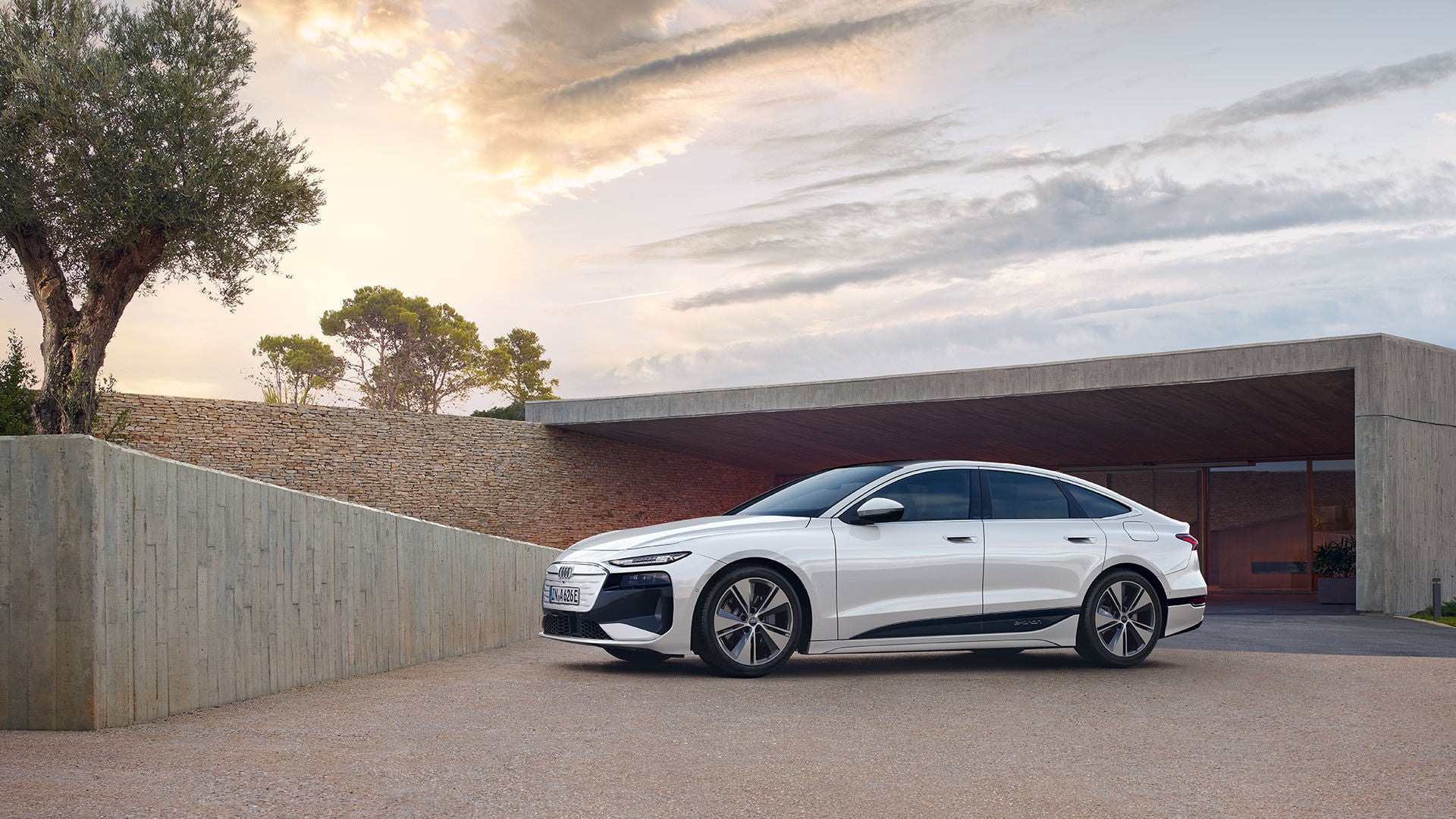 Three-quarter side view of the Audi A6 e-tron parked next to a modern house.