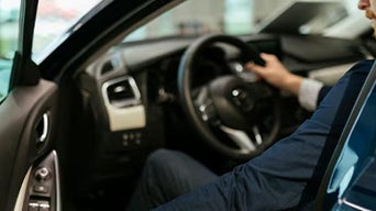 Person in a blue suit sitting in a car, adjusting the steering wheel.