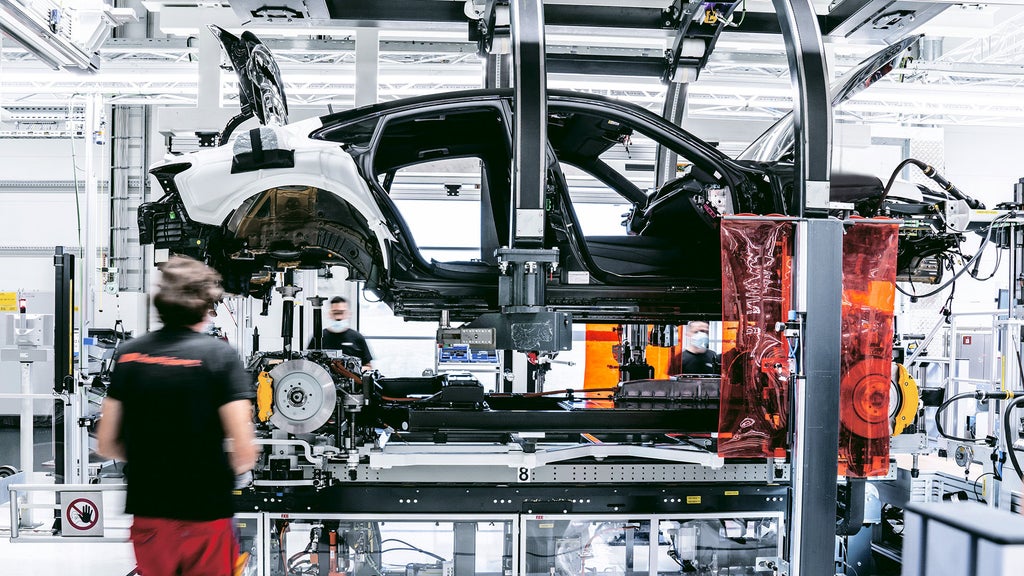 Two Audi technicians assembling the body, battery, electric motors, and suspension of the Audi e-tron GT inside the production plant.