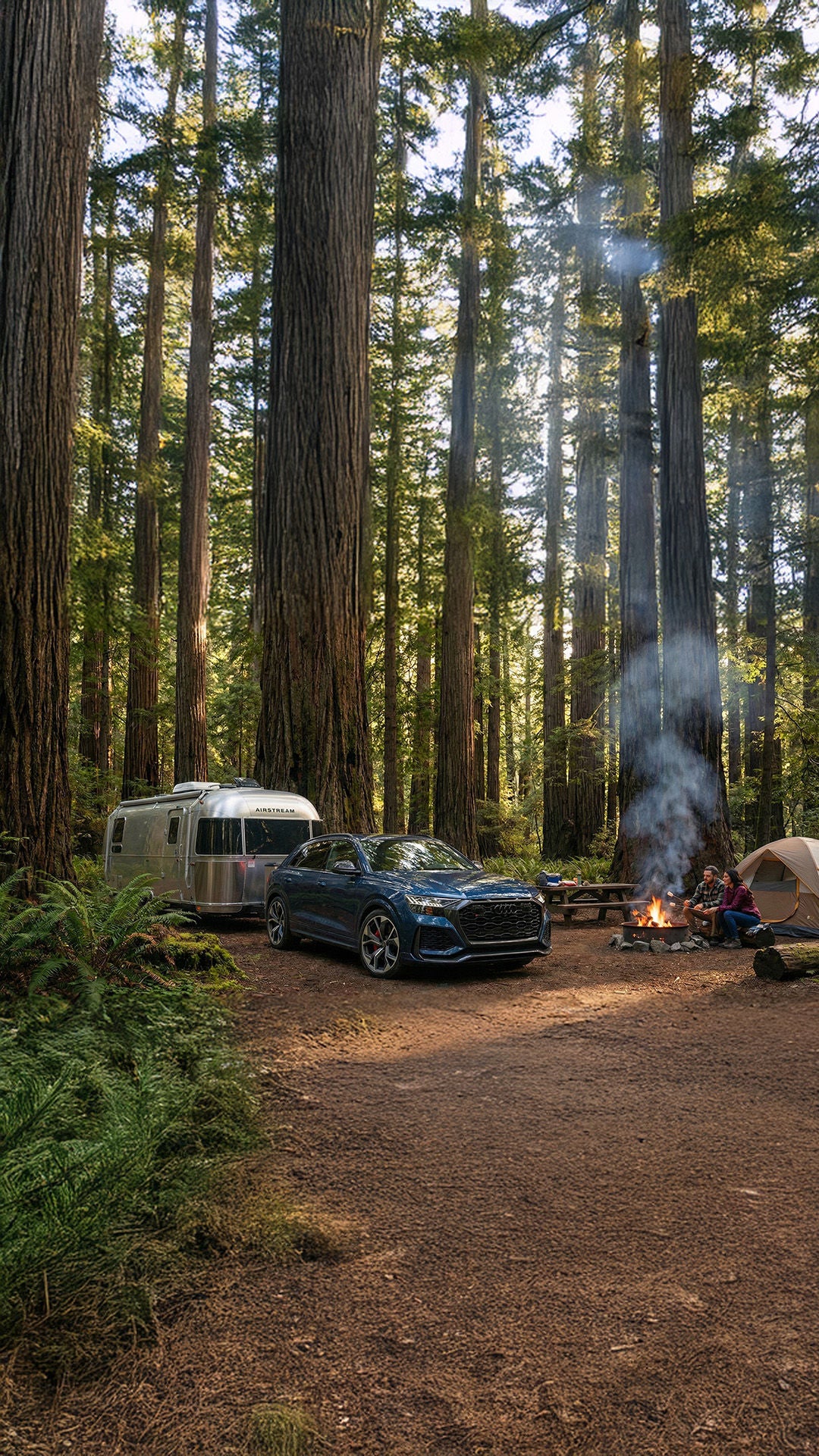 2026 Audi Q8 towing an Airstream at a campsite in redwood forest with couple sitting by a fire
