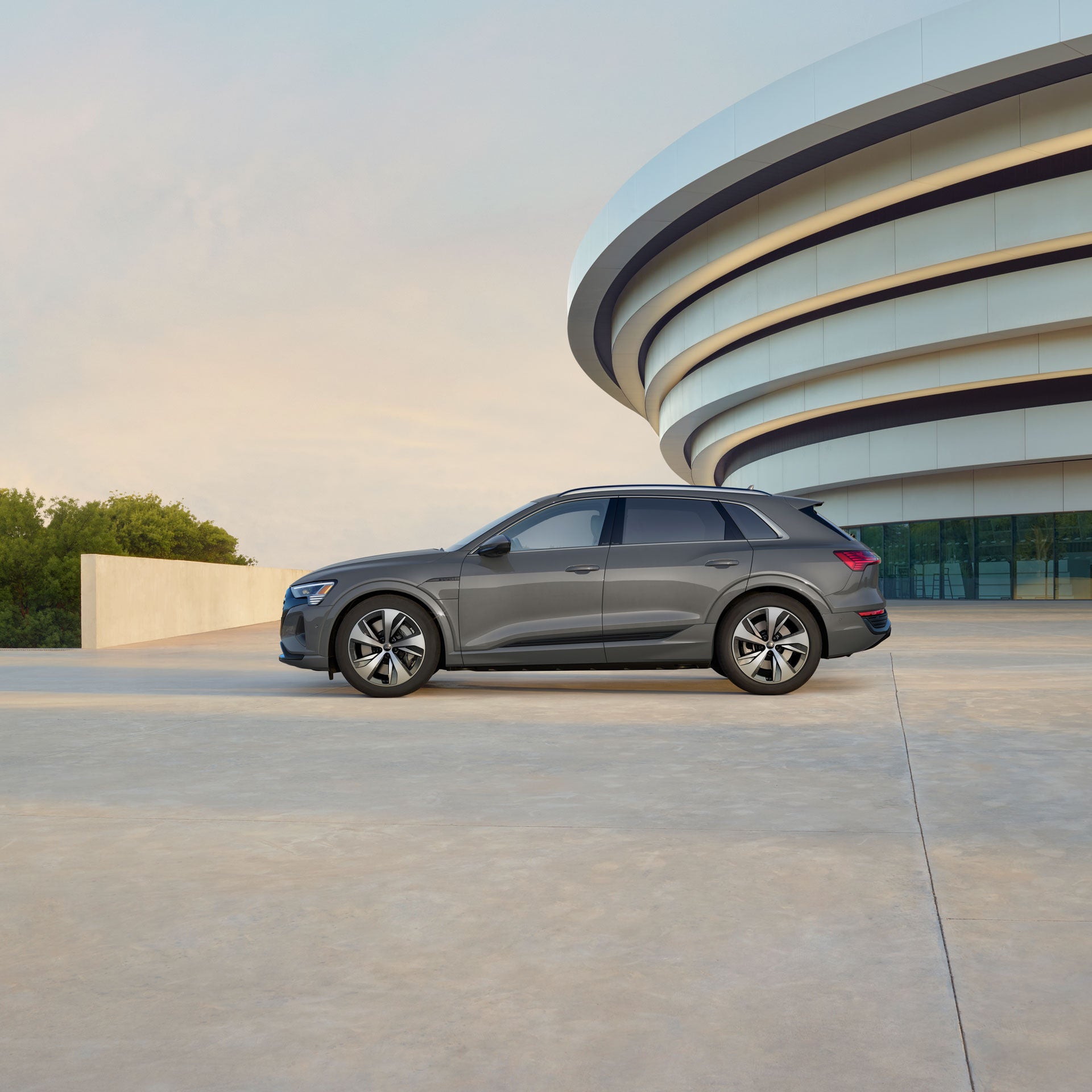 Profil latéral d'une Audi Q8 e-tron grise garée près d'un bâtiment moderne.