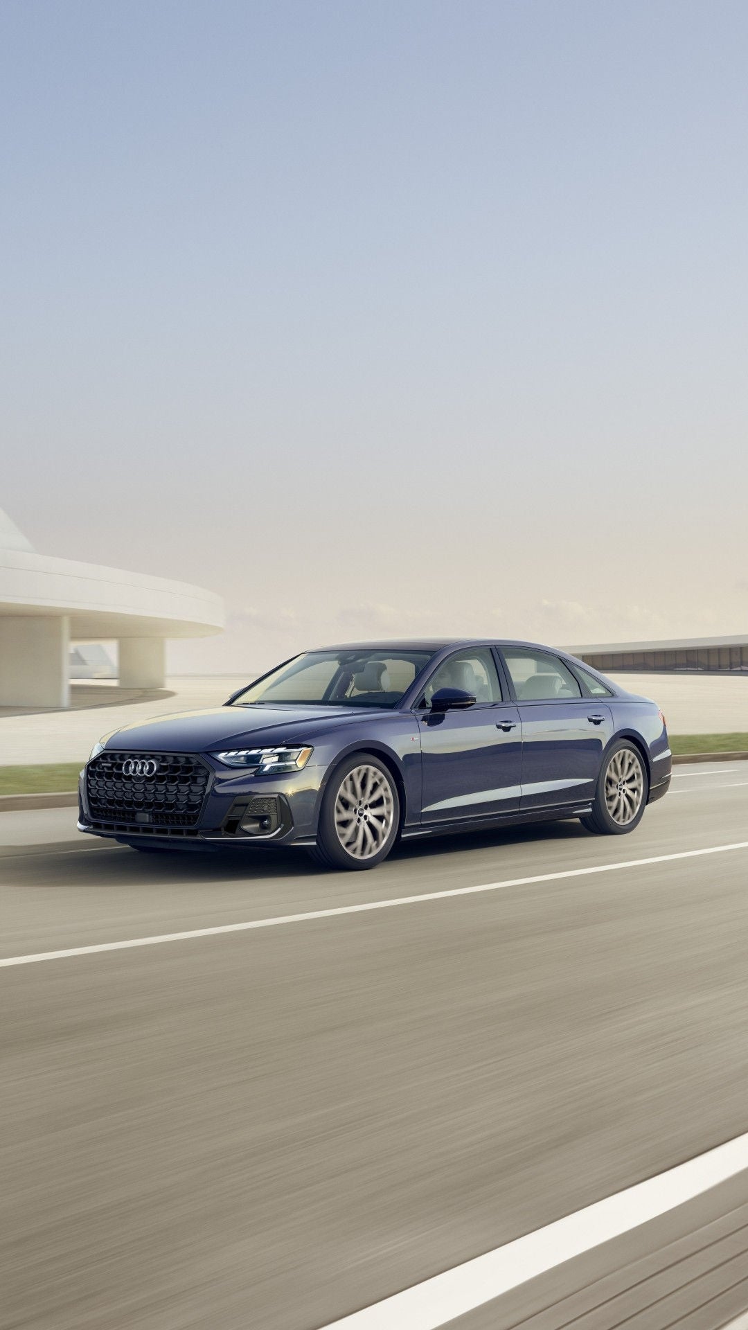 3/4 front view of an Audi A8 driving in front of a modern building.
