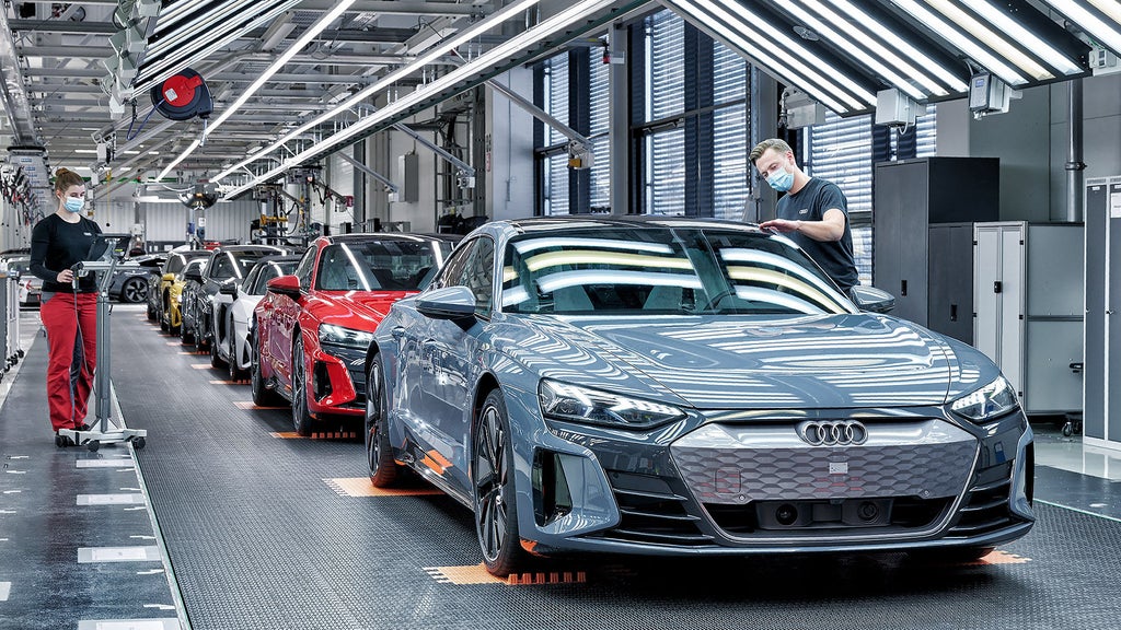 Two Audi technicians performing the final quality check on a range of differently-colored Audi e-tron GTs on the assembly line.