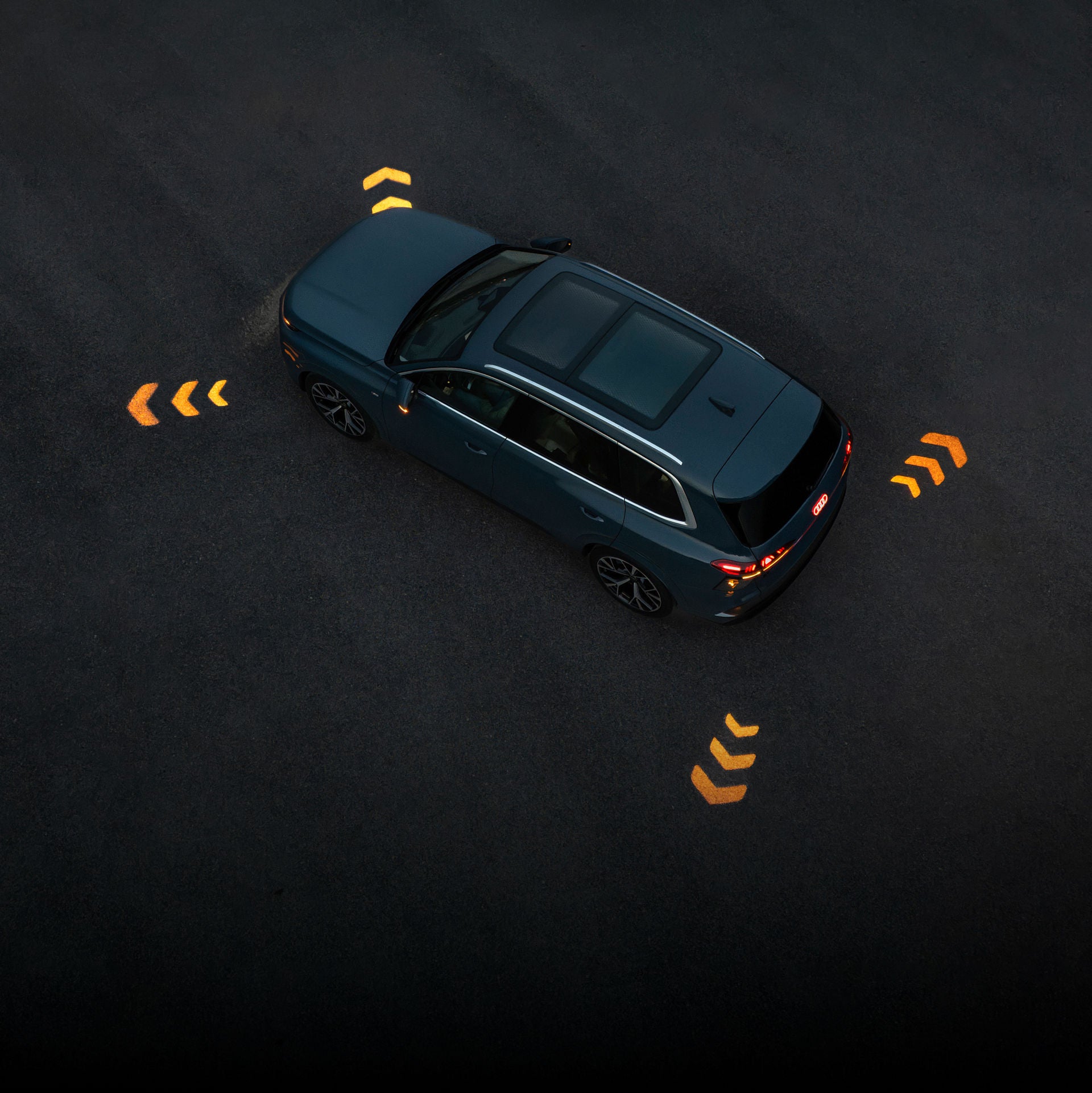 Aerial view of an Audi vehicle with signal indicator lighting projections on the ground surrounding the vehicle.