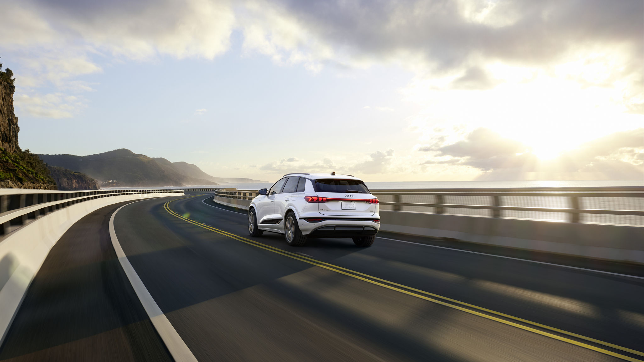 White q6 e-tron driving away on the road with a sunrise. 