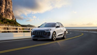 Three-quarter front view of the Audi Q6 e-tron accelerating on a hillside road.