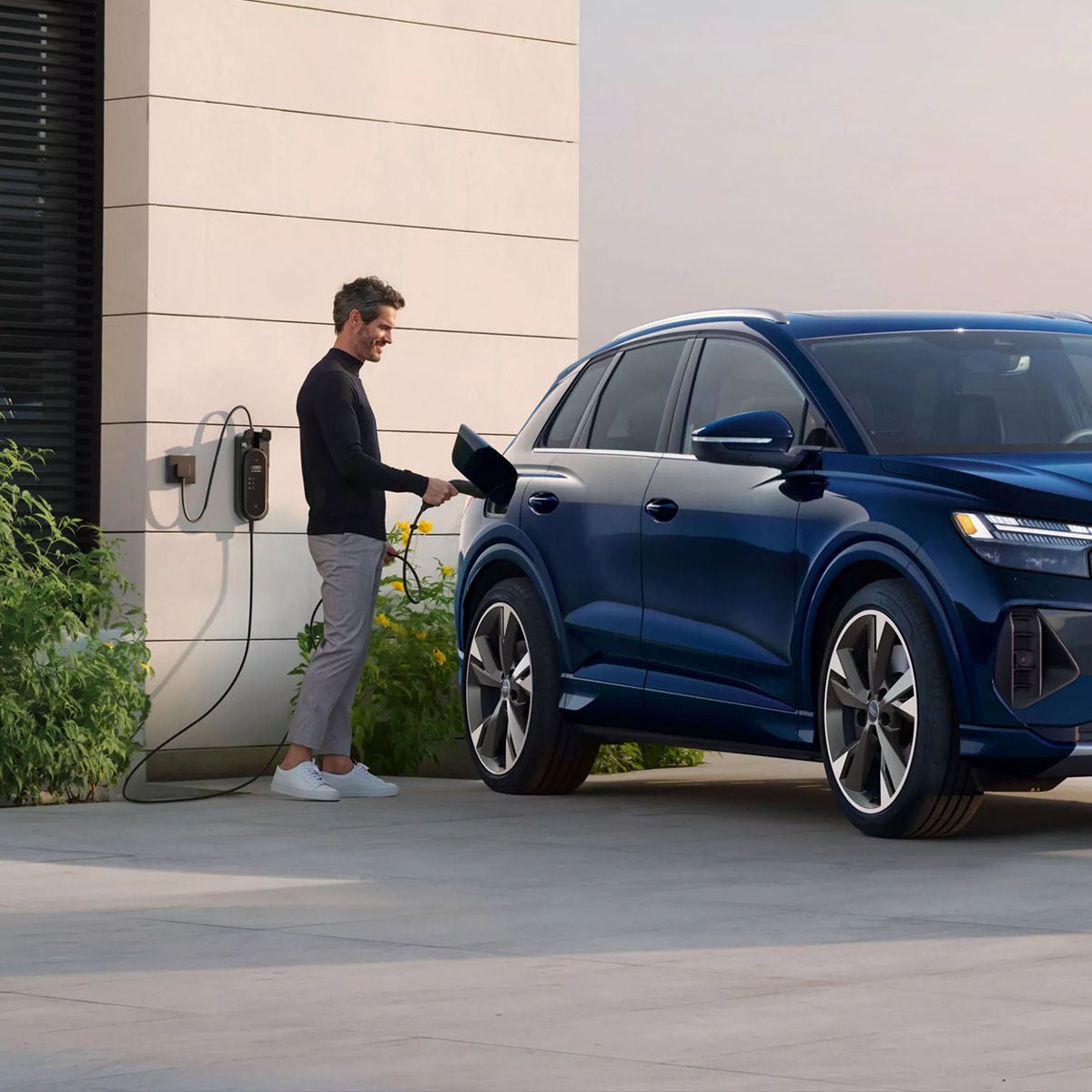 A man charging his Audi Q4 Sportback e-tron in front of a modern home.
