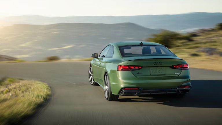 A bright green Audi sedan driving through a mountain road.