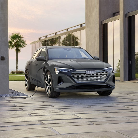 Three-quarter frontal view of an Audi Q8 e-tron plugged into a charger.