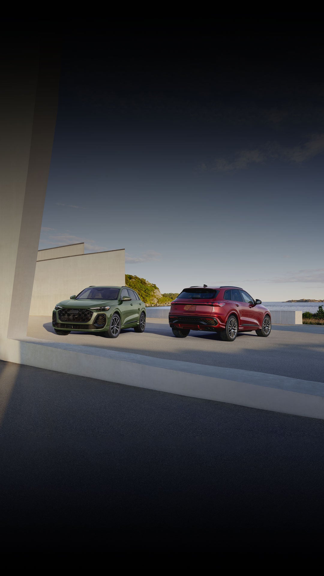 Two Audi SUV models parked by a waterfront.