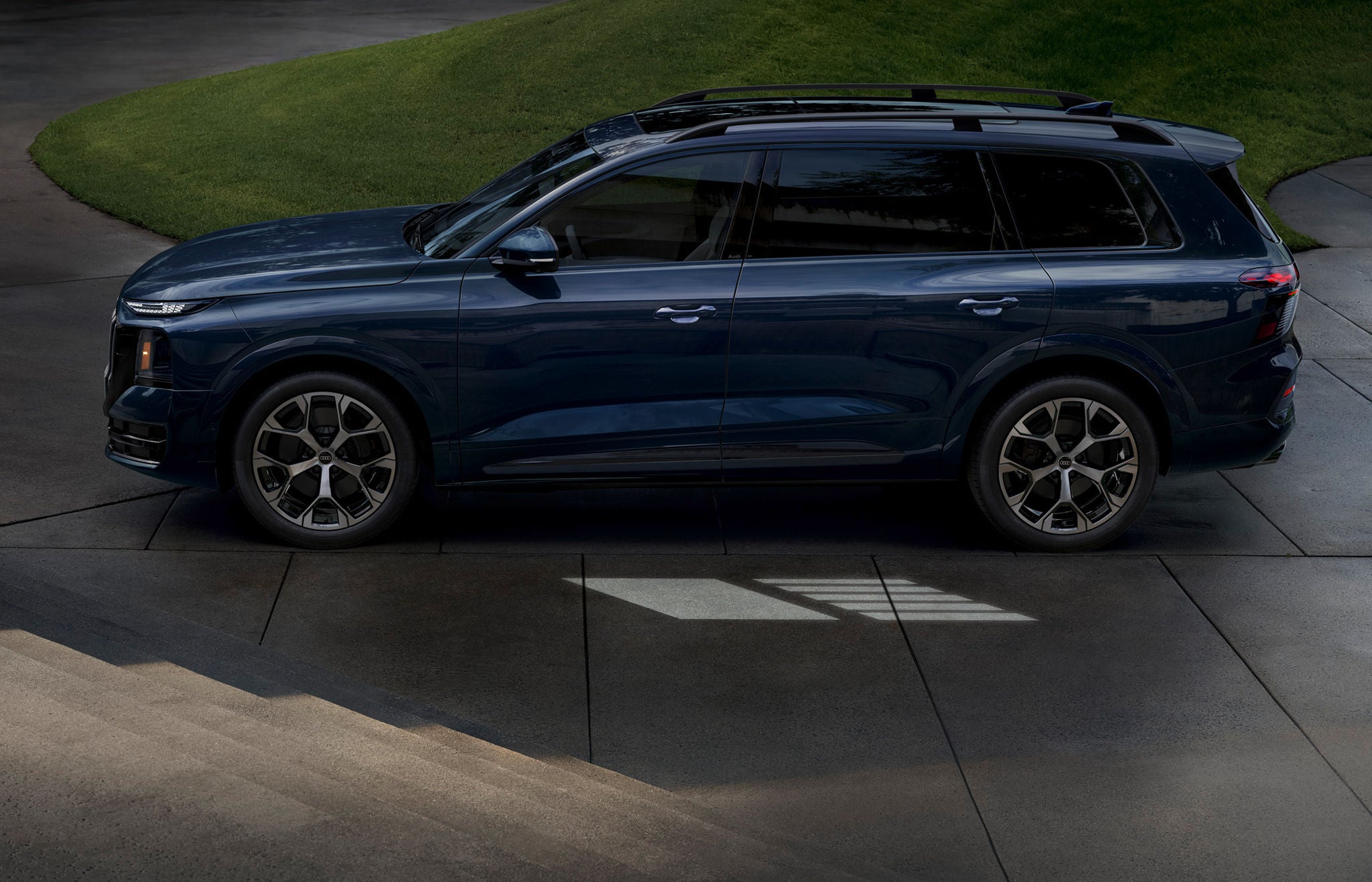 Side profile of a dark blue 2027 Audi Q9 luxury SUV parked on a modern driveway.