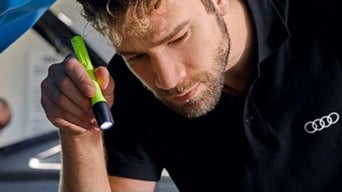 Service technician inspecting an Audi vehicle with a flashlight.
