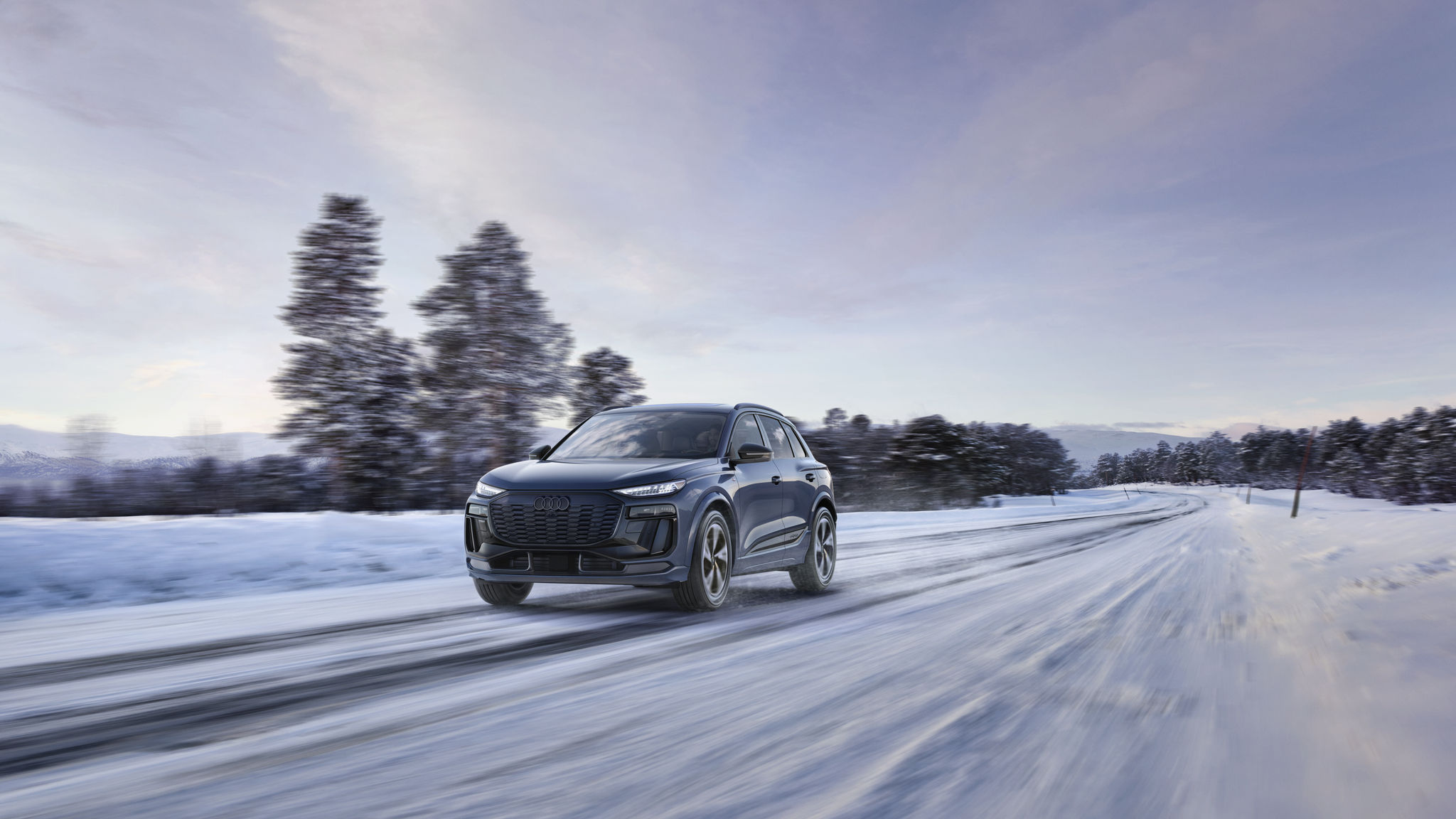 Black 2027 q6 e-tron driving on light snow with trees in the background. 