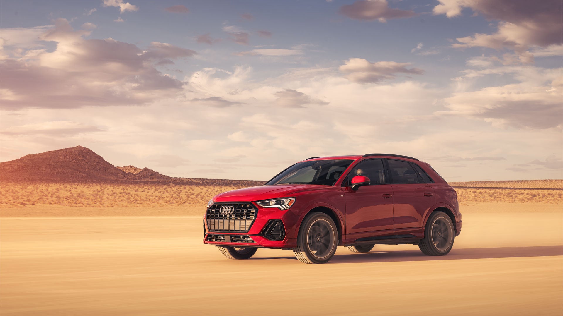 Three-quarter front view of the Audi Q3 parked in a sandy landscape.
