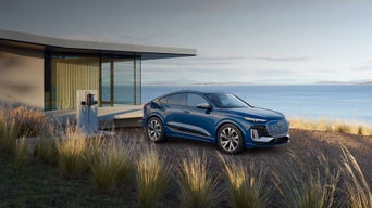 Three-quarter side view of the Audi SQ6 Sportback e-tron parked and charging by a waterside home.