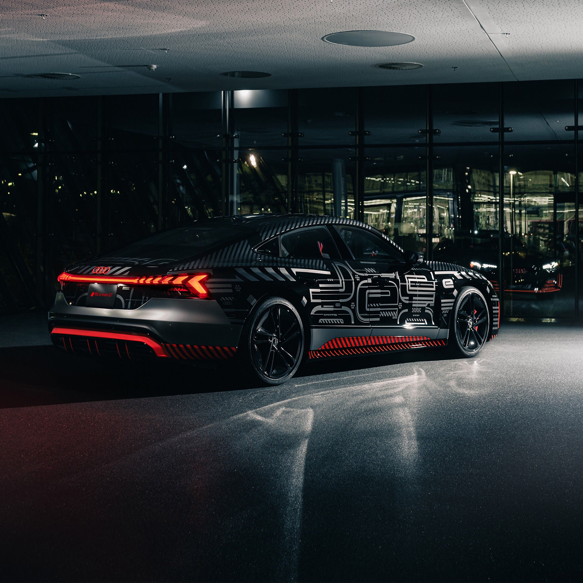 Three-quarter rear view of the Audi RS e-tron GT project 513/2 parked inside of a glass building at night.