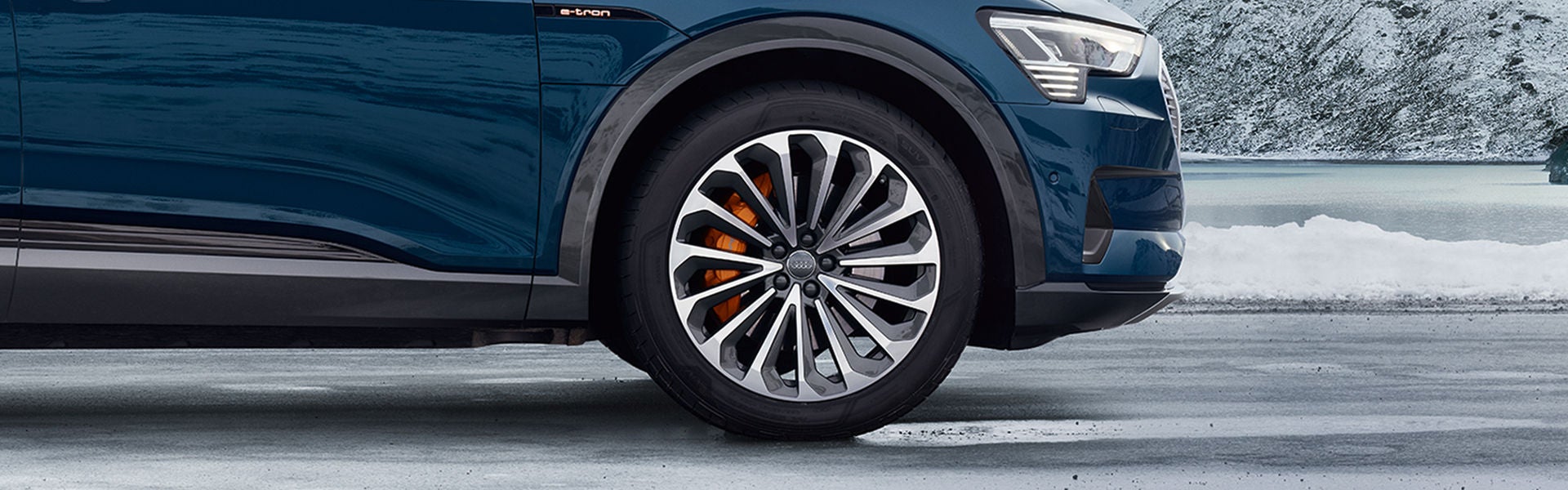 Close-up side profile of an Audi e-tron driving on a snowy road. 