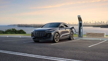 Three-quarter front view of the Audi Q6 Sportback e-tron parked and charging by a waterfront.