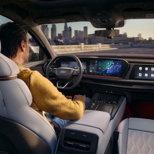 Close-up of a display in the vehicle interior. The silhouette of a vehicle travelling straight ahead is shown. To the left is a text box providing information about assisted hands-free driving.