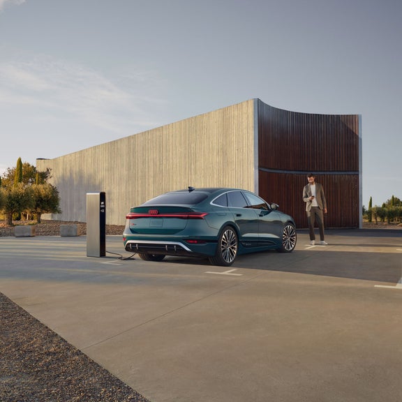 Three-quarter rear view of the Audi S6 e-tron parked and charging with a person standing nearby.