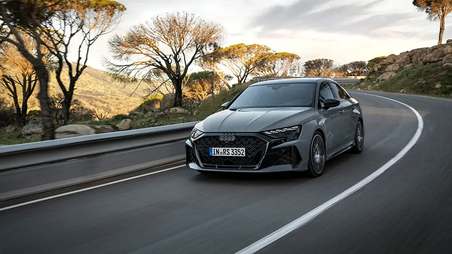 Vue avant de l'Audi RS3 grise qui roule sur une route sinueuse en montagne.