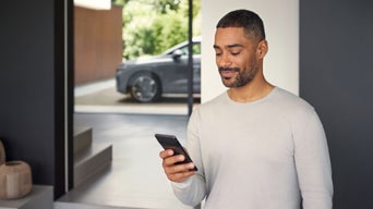A man is looking at his phone screen. An Audi model is parked in the background.