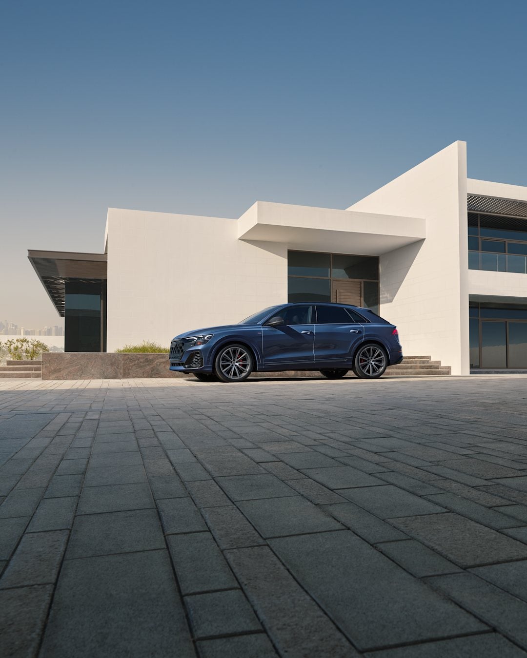 Front three-quarter view of an Audi Q8 in blue parked in front of a modern white house.