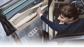 A person opening the driver door of an Audi, showing the Audi rings entry light cast on the ground.