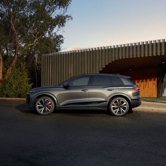 Plan latéral d’un Audi SQ6 e-tron stationné devant un bâtiment moderne.