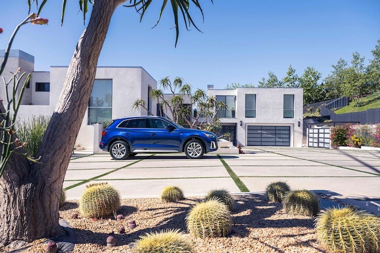 Blue SUV parked in front of a modern home with desert landscaping.