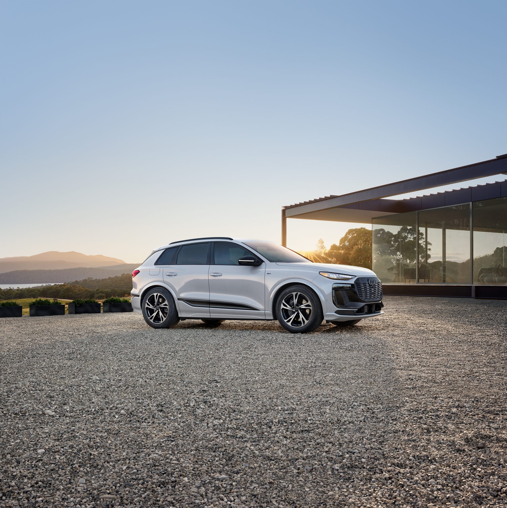 White q6 e-tron on gravel with a sunset and mountains in the background. 