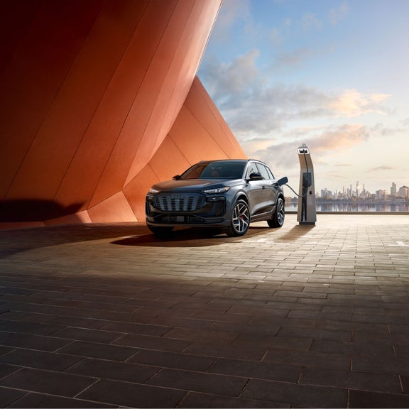 Three-quarter front view of the Audi SQ6 e-tron parked and charging by a modern building.