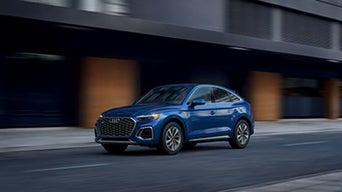 Blue Audi SUV driving through a modern city street.