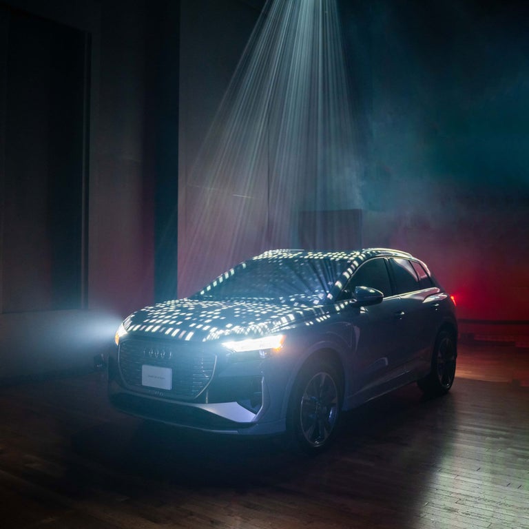 The Audi Q4 e-tron parked inside a dark room, illuminated by spotlights.
