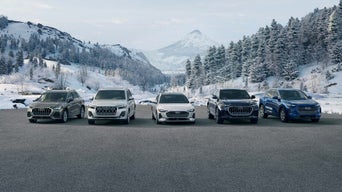 A woman gets into an Audi driving experience vehicle. The instructor stands next to the vehicle on the passenger side.