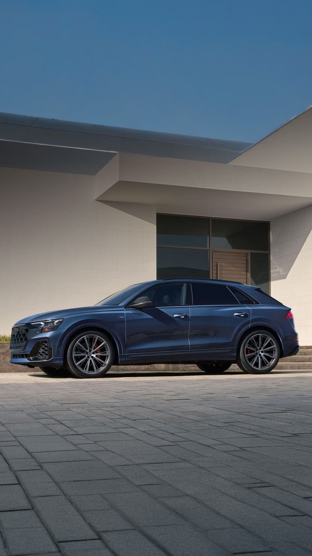 Side profile of the Audi Q8 parked in front of a modern home.