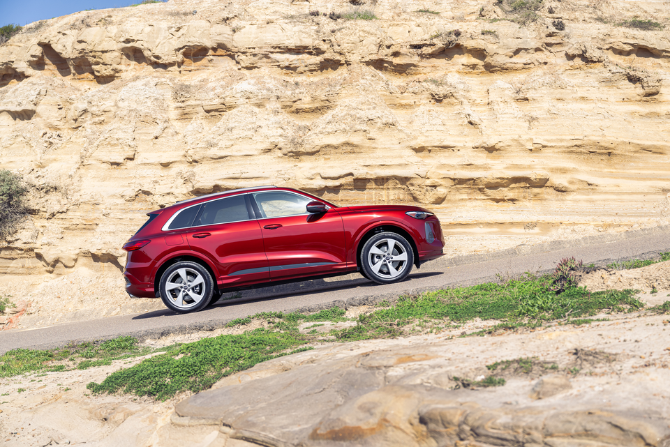 Red Audi Q5 driving upwards on rocky road positioned on an incline.