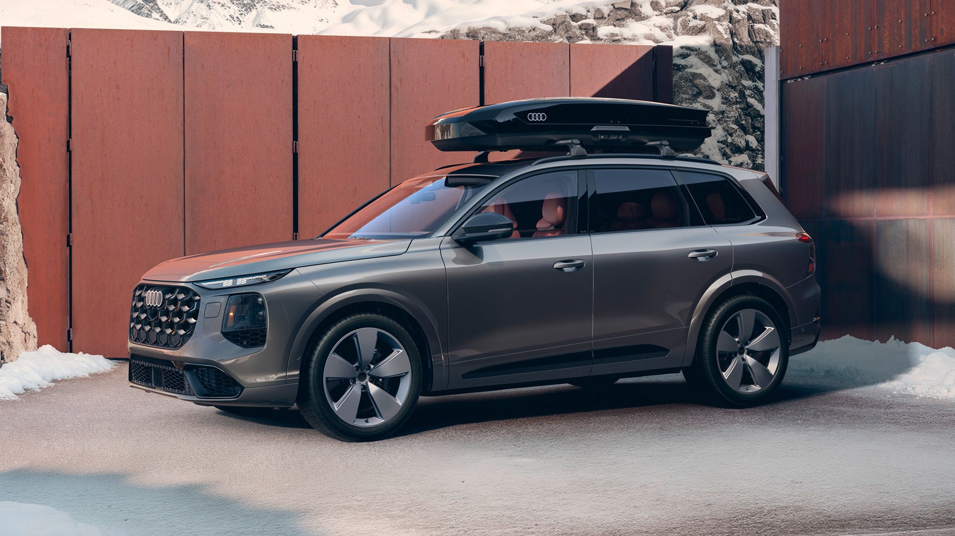 The Audi SQ7 SUV is parked in front of a modern residential building. There is a roof box on the vehicle.
