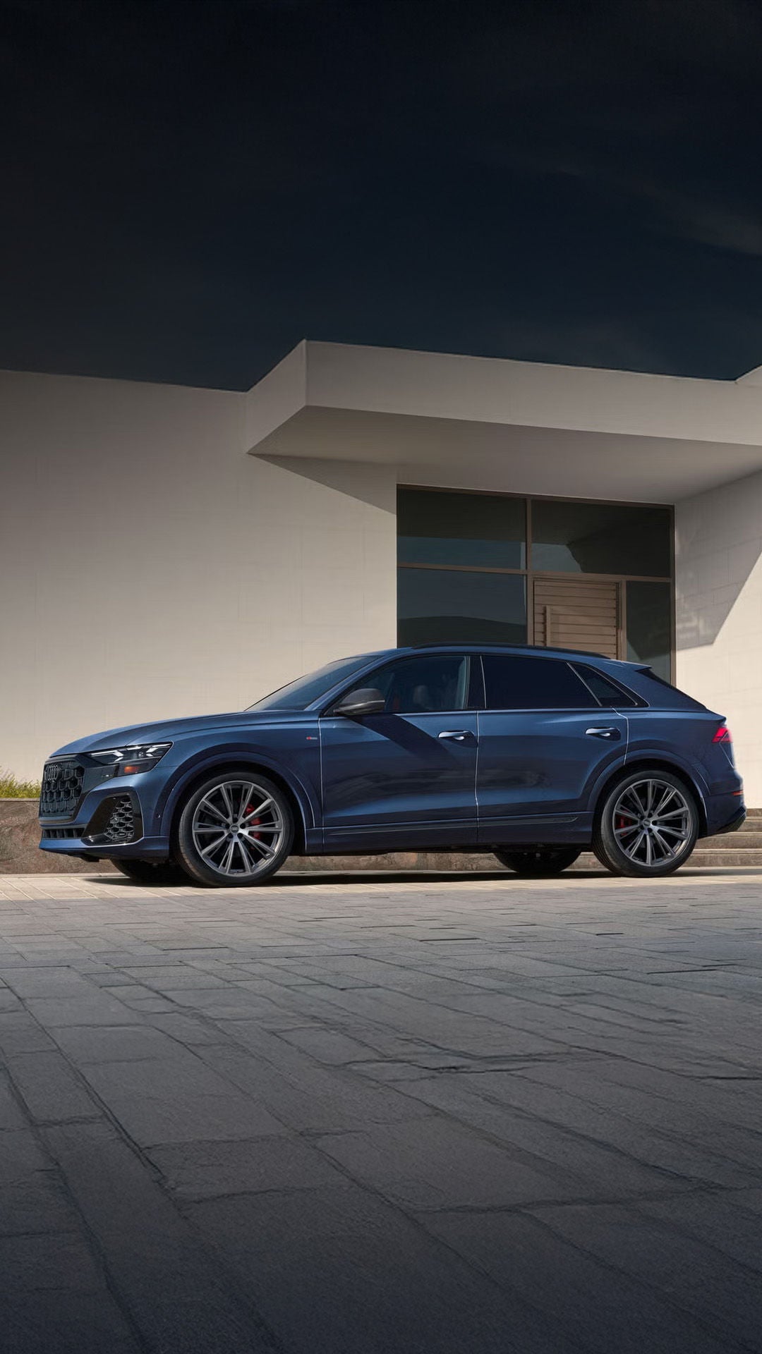 Side profile of the Audi Q8 parked in front of a modern home.