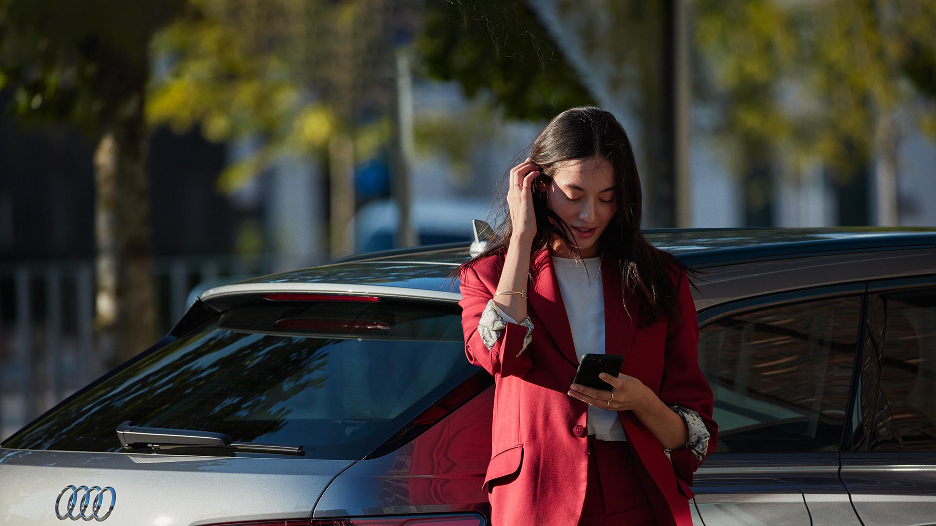 Une femme appuyée contre un véhicule Audi utilisant son téléphone portable.